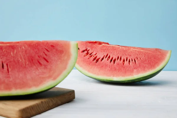 Nahaufnahme arrangierter Wassermelonenscheiben auf Schneidebrett und weißer Oberfläche auf blauem Hintergrund — Stockfoto