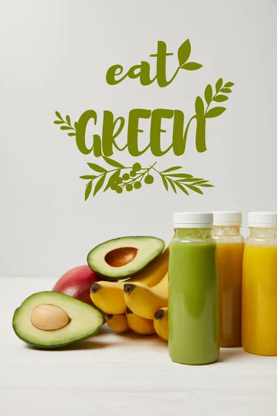 Frutas frescas de desintoxicación y batidos en botellas sobre fondo blanco, comer inscripción verde - foto de stock