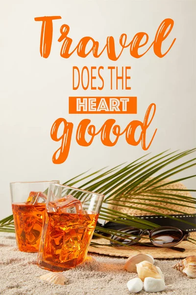 Close up view of straw hat, cocktails, seashells, sunglasses and palm leaf on sand on grey backdrop, travel does heart good inscription — Stock Photo