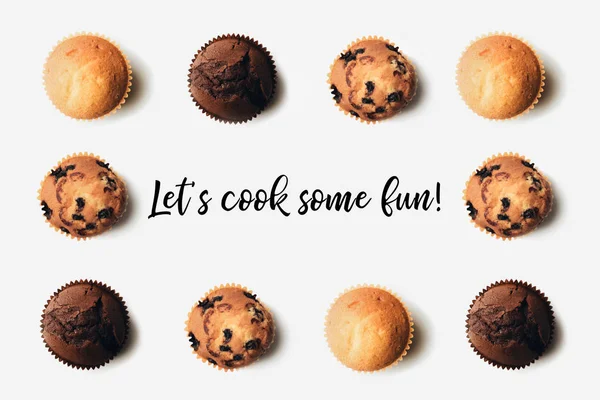 Top view of arranged freshly baked delicious muffins on white, lets cook some fun inscription — Stock Photo