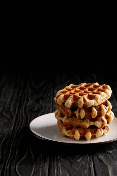 Pila di waffle belgi appena sfornati su piatto su tavolo di legno nero — Foto stock