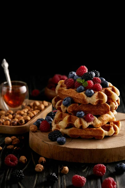 Waffles belgas deliciosos com bagas e avelãs na mesa de madeira preta — Fotografia de Stock