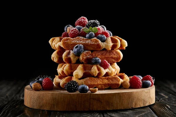 Pila appena sfornata di cialde belghe con bacche su tagliere di legno su nero — Foto stock