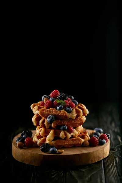 Tasty stacked belgian waffles with berries on wooden cutting board on black — Stock Photo