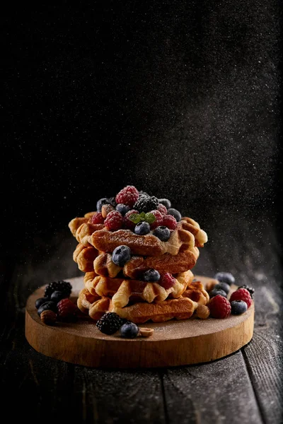 Waffles belgas deliciosos com açúcar em pó derramando de lado no preto — Fotografia de Stock