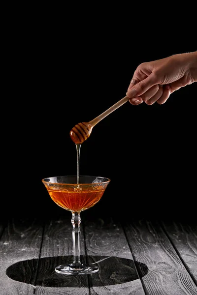 Tiro recortado de la mujer vertiendo miel en el vidrio sobre la mesa de madera negro - foto de stock