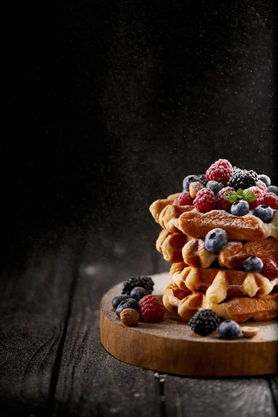 Waffles belgas saborosos com açúcar em pó derramando de lado no preto — Fotografia de Stock