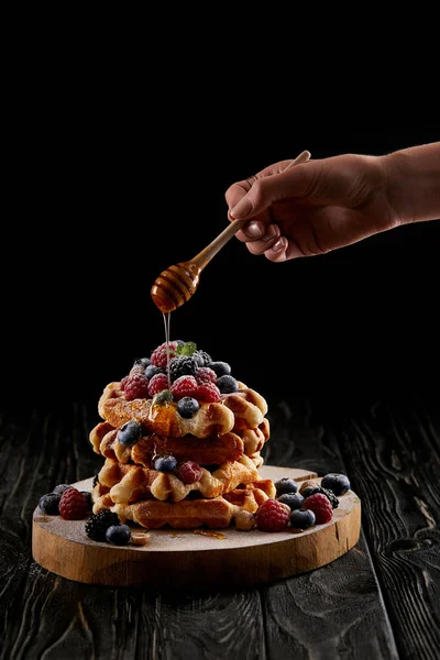 Tiro cortado de mulher derramando mel na pilha de waffles belgas em mesa de madeira preta — Fotografia de Stock