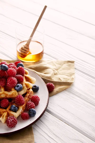 Waffles belgas saborosos com bagas e vidro de mel na mesa de madeira branca — Fotografia de Stock