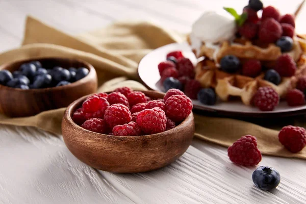 Bowls with berries with belgian waffles blurred on background on white wooden table — Stock Photo