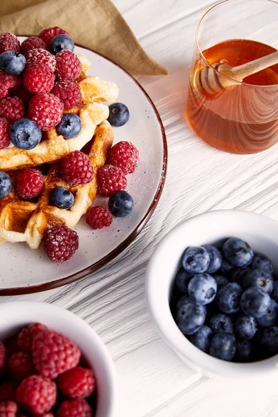 Close-up shot of delicious belgian waffles with berries and honey on white wooden table — Stock Photo