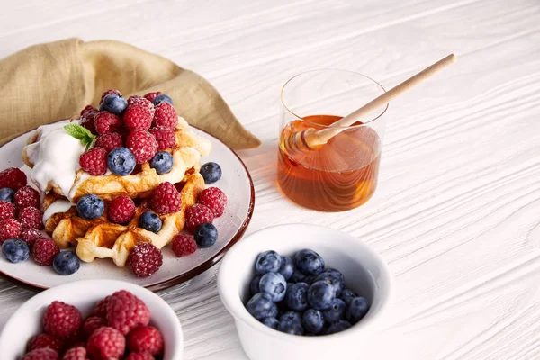 Вкусные бельгийские вафли с ягодами и медом на белом деревянном столе — стоковое фото