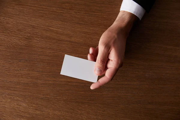 Cropped image of businessman giving blank business card at wooden table — Stock Photo