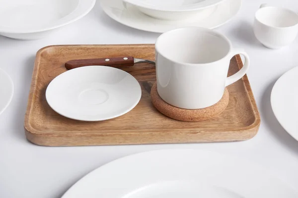 Close up view of wooden tray, various plates and bowl with cup on white table — Stock Photo