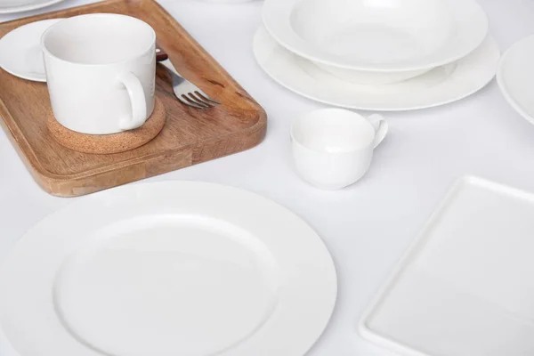 Vista de cerca de la bandeja de madera, tenedor con varios platos y taza con tazón en la mesa blanca - foto de stock