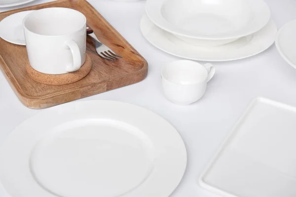 Close up view of wooden tray, fork with various plates and cup with bowl on white table — Stock Photo