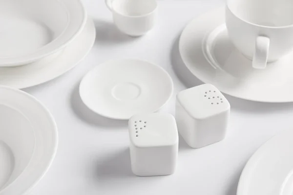Селективный фокус различных тарелок, чашки, миски, соляной погреб и перец на белом столе — стоковое фото