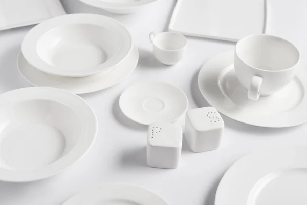 Close up view of different plates, cup, bowl, saltcellar and pepper caster on white table — Stock Photo