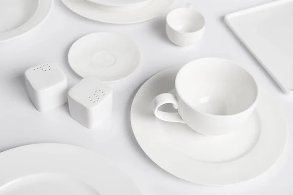 Close up image of different plates, cup, bowl, saltcellar and pepper caster on white table — Stock Photo