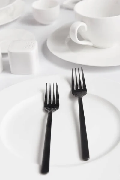 Vue rapprochée des fourchettes, des assiettes diverses et de la cave à sel sur table blanche — Photo de stock