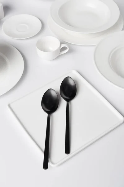 Selective focus of various plates, two spoons and cup on white table — Stock Photo