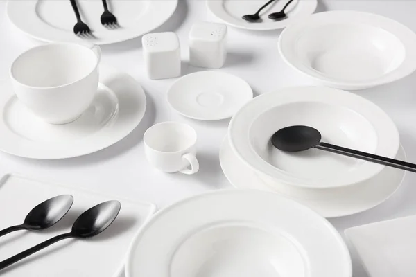 Selektiver Fokus verschiedener Teller, Tasse, Schüssel, Salatlöffel, Salzkeller und Pfefferstreuer, Gabeln mit Löffeln auf weißem Tisch — Stockfoto