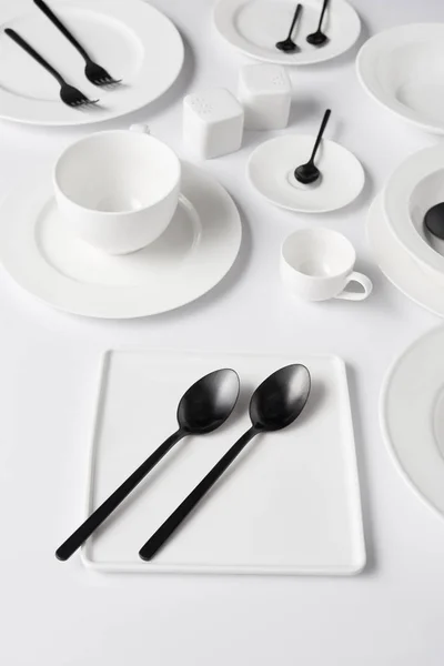 Selective focus of different plates, cup, bowl, salt pot and pepper caster, forks with spoons on white table — Stock Photo