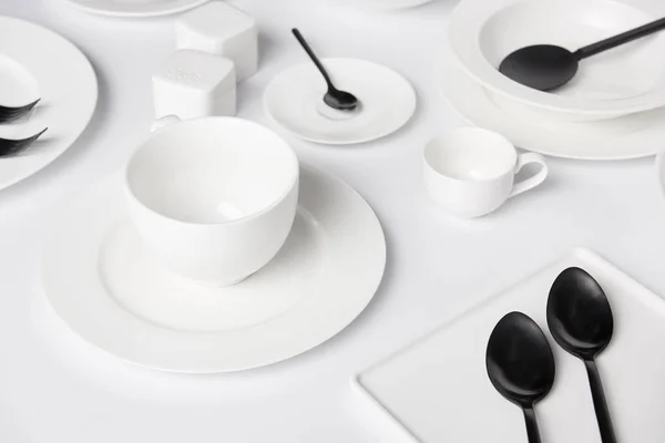 Selective focus of different plates, cup, bowl, salad spoon, saltcellar and pepper caster, forks with spoons on white table — Stock Photo