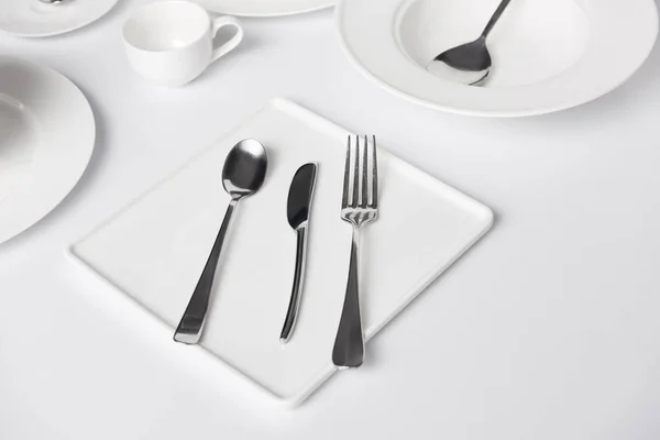Foco seletivo de várias placas, copo, garfo, faca e colheres na mesa branca — Fotografia de Stock