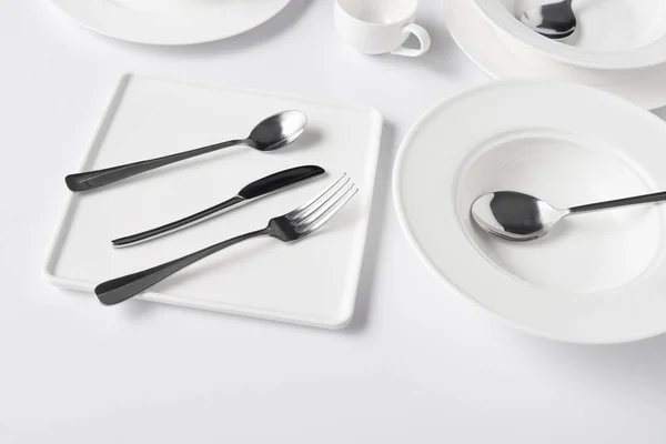 Cerrar vista de varios platos, taza, tenedor, cuchillo y cucharas en la mesa blanca - foto de stock