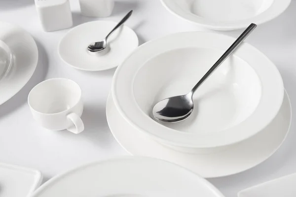 Enfoque selectivo de cucharas, diferentes platos y taza en la mesa blanca - foto de stock