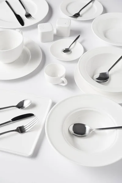 Вибірковий фокус на різних тарілках, чашці, мисці, солоному горщику та перцю, ножах, виделках з ложками на білому столі — стокове фото