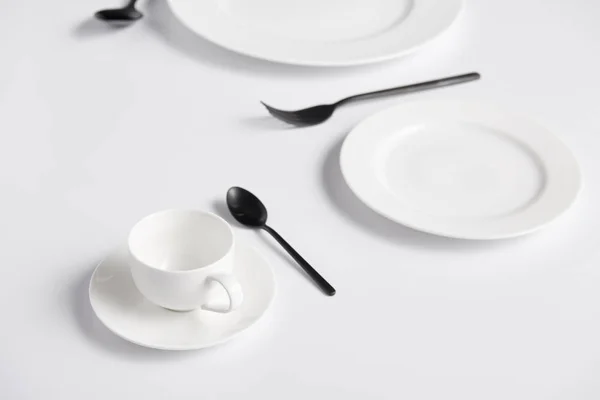 Selective focus of cup, spoons, fork and various plates on white table — Stock Photo
