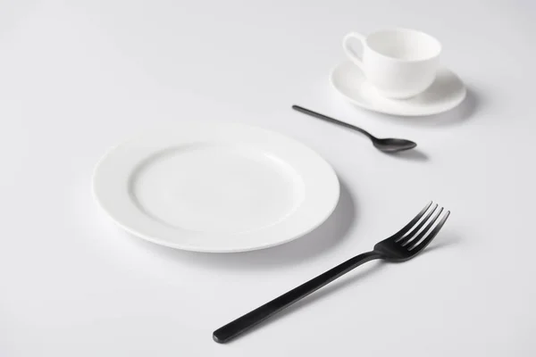 Enfoque selectivo de la placa, tenedor, cuchara y taza en la mesa blanca - foto de stock