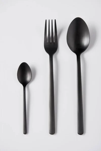 Elevated view of black spoons and fork on white background, minimalistic concept — Stock Photo