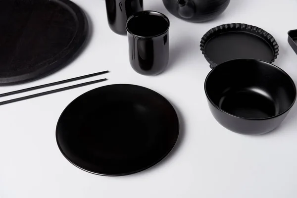 Selective focus of black plate, bowl, cups, chopsticks, baking dish and tray on white table — Stock Photo