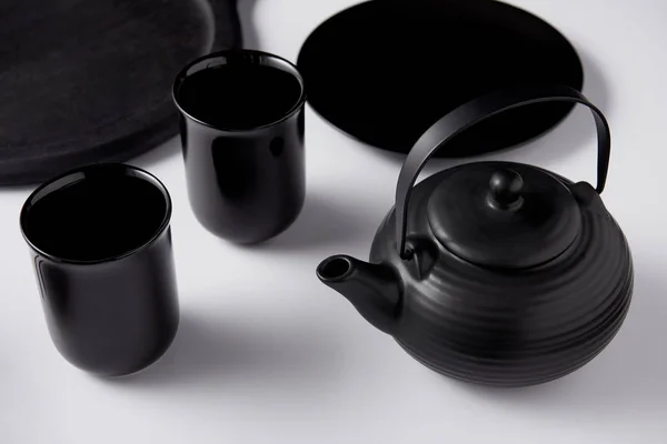 Selective focus of black teapot, cups, plate and tray on white table — Stock Photo