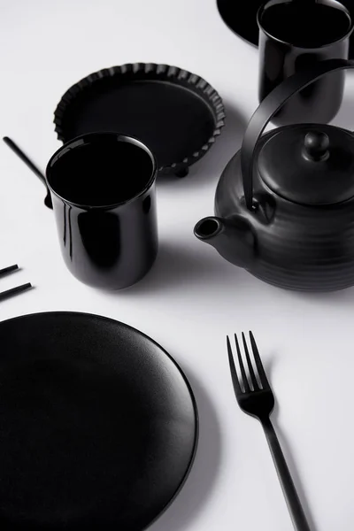 Close up view of black teapot, plate, cups, fork, chopsticks and baking dish on white table — Stock Photo