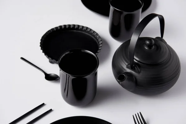 Enfoque selectivo de la tetera negra, tazas, tenedor, cuchara, palillos y bandeja para hornear en la mesa blanca - foto de stock