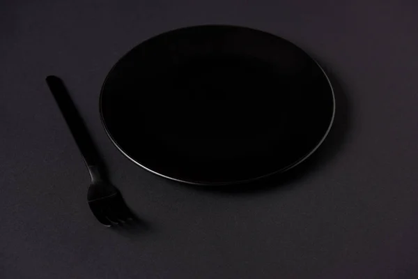 Селективный фокус черной пластины и вилки на черном столе, минималистическая концепция — стоковое фото