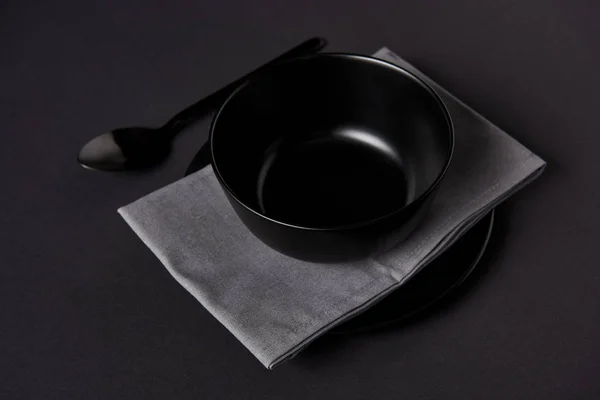 Enfoque selectivo de cuenco negro, cuchara, toalla de cocina y plato en mesa negra - foto de stock