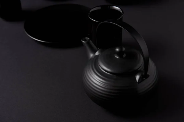 Selective focus of black teapot, cups and plate on black table — Stock Photo