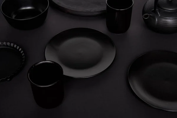 Selective focus of black teapot, bowl, baking dish, cups and plates on black table — Stock Photo