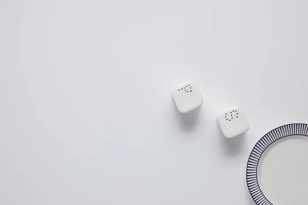 Vista superior de la placa, bodega de sal y echador de pimienta en la mesa blanca, concepto minimalista - foto de stock