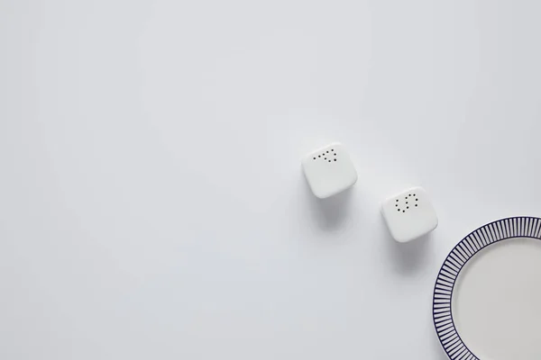 Top view of plate, saltcellar and pepper caster on white table, minimalistic concept — Stock Photo