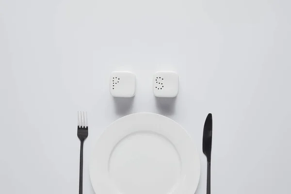 Vista dall'alto di piatto, forchetta, coltello, saliera e pepe rotella su tavolo bianco, concetto minimalista — Foto stock