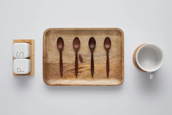 Vista dall'alto del vassoio in legno con cucchiai, saliera, macchina per colata continua del pepe e tazza sul tavolo bianco — Foto stock