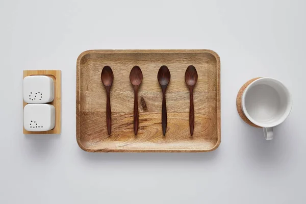 Top view of arranged wooden tray with spoons, saltcellar, pepper caster and cup on white table — Stock Photo