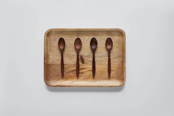 Vue de dessus du plateau en bois avec cuillères en bois sur table blanche, concept minimaliste — Photo de stock