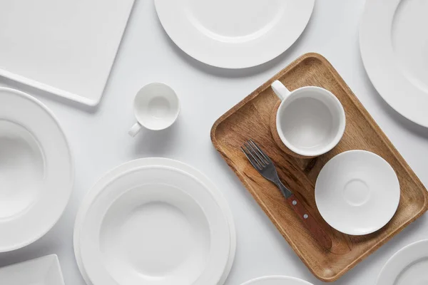 Vue du dessus de la tasse, différentes assiettes, plateau en bois, bol et fourchette sur table blanche — Photo de stock